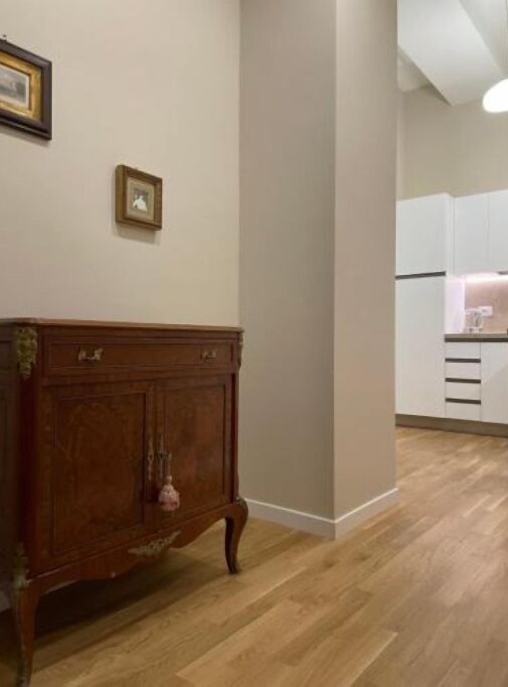 Une pièce avec un meuble en bois, un tableau encadré au mur et un coin cuisine avec des meubles blancs.