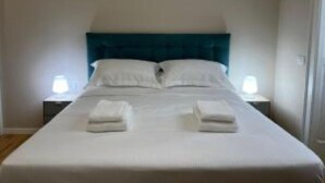 Una cama individual con cabecera color turquesa, ropa de cama blanca y dos lámparas de noche.