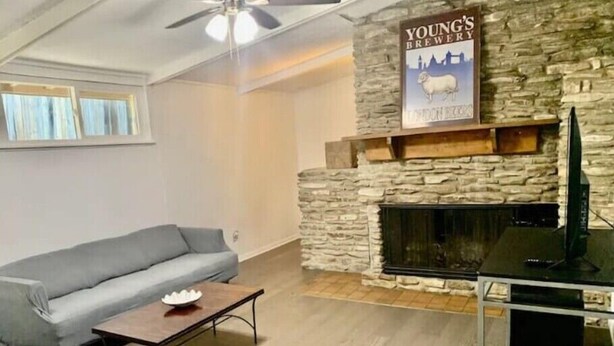A living room with a stone fireplace, a grey sofa, a coffee table, and a television. - Central & spacious 3bed Near Airport & Downtow

 (Austin)