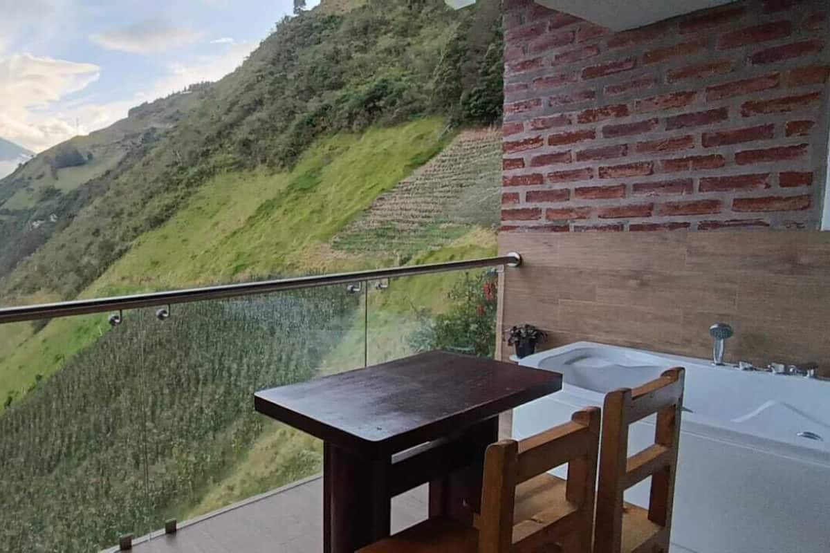 Un balcón con vistas a un paisaje montañoso, un muro de ladrillo y una mesa de madera con una silla.