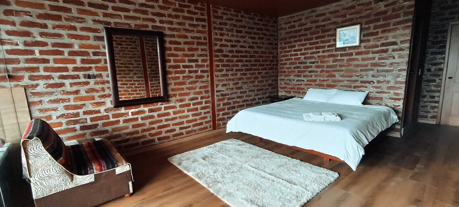 Quarto com parede de tijolos, cama com roupa de cama branca, piso de madeira e tapete branco.
