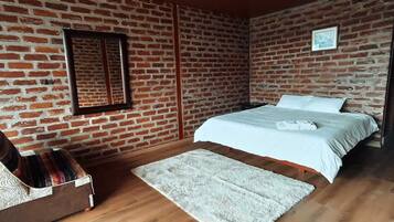 Quarto com parede de tijolos, cama com roupa de cama branca, piso de madeira e tapete branco.