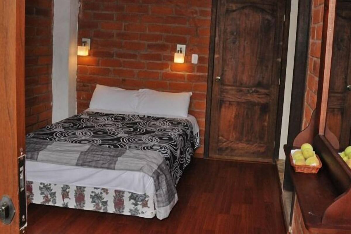 Una habitación pequeña y acogedora con una cama, una puerta de madera y un pequeño banco con manzanas.
