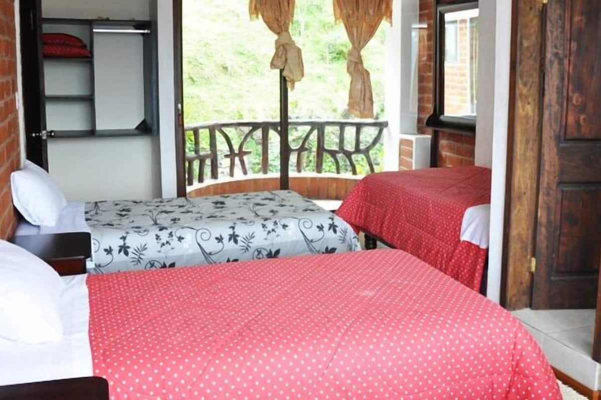 Una habitación con dos camas, un banco de madera, una mesita y una ventana con vistas a follaje.