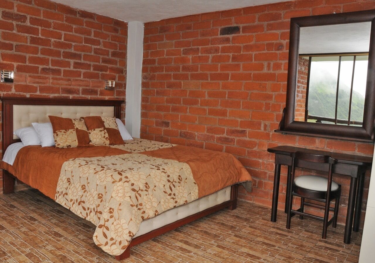 Una camera da letto con una parete in mattoni, un letto con copripiumino floreale, un comodino e una sedia.