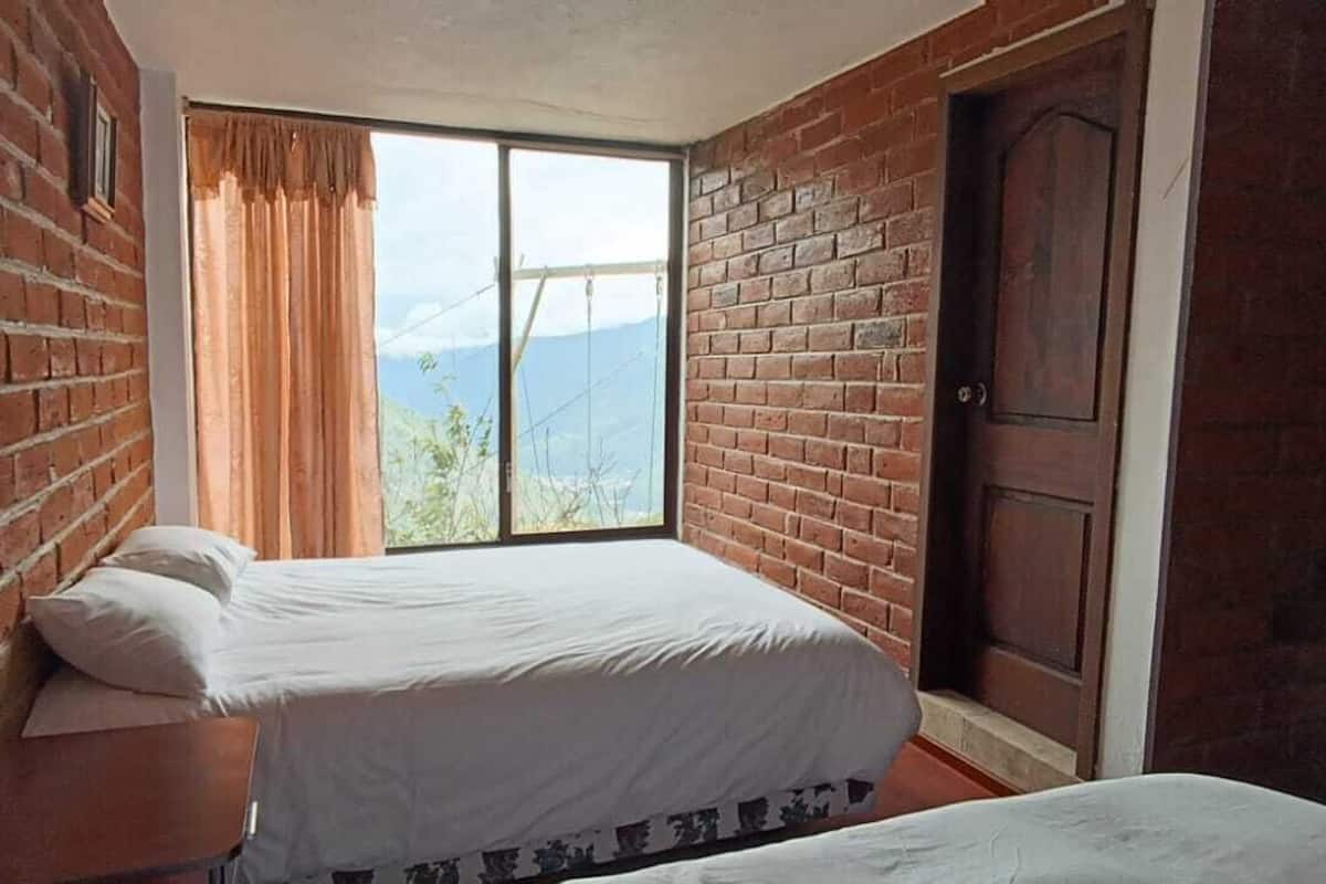 Una habitación con cama, ventana con cortinas, pared de ladrillo y puerta de madera.