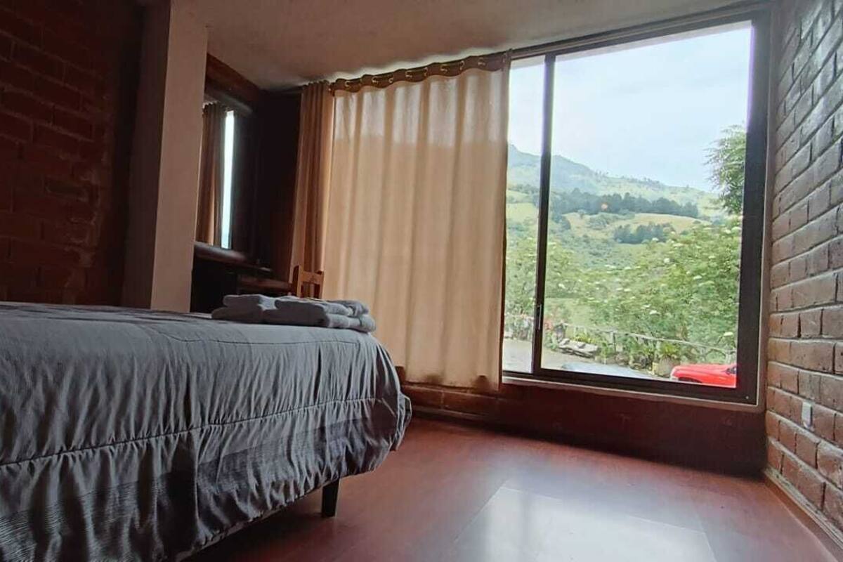 Un dormitorio con cama, ventana con cortinas y vistas a un paisaje montañoso.