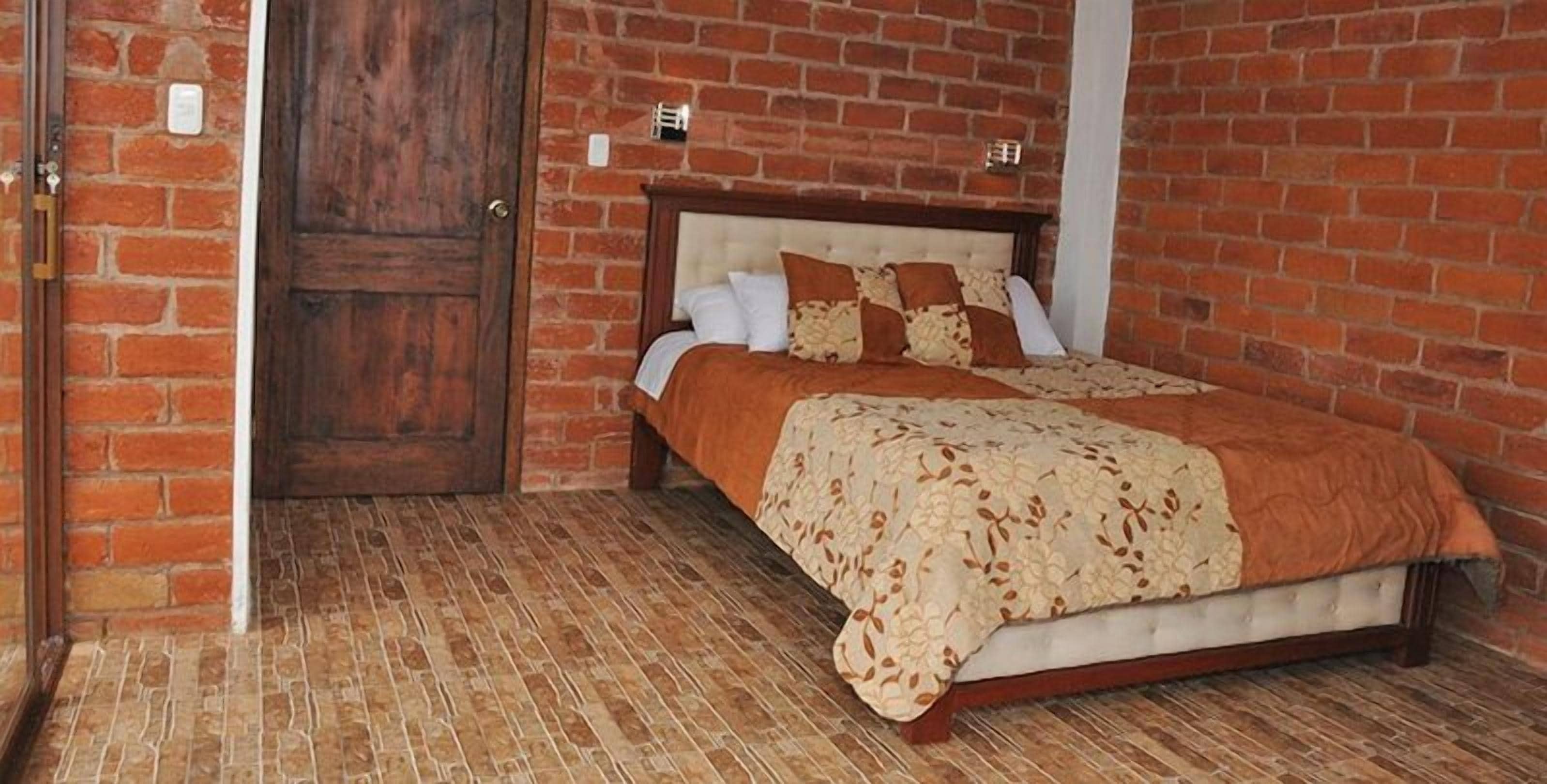 A bedroom with a brick wall, a wooden door, a bed with a floral bedspread, and a white headboard.