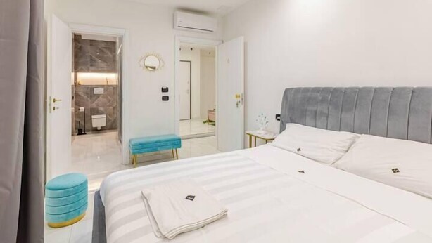 Une chambre d’hôtel avec un grand lit, une table de chevet, un miroir et une salle de bain visible à travers une porte ouverte.