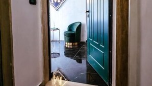 L’entrée d’un hôtel, avec une porte de couleur turquoise, un paillasson noir orné d’un monogramme et une enseigne fixée au mur, sur laquelle figure une grande lettre « M ».