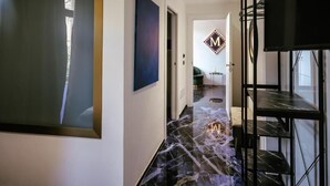 Un couloir doté d’un sol en marbre, une grande œuvre d’art encadrée sur le côté gauche et une étagère en métal noir sur le côté droit.