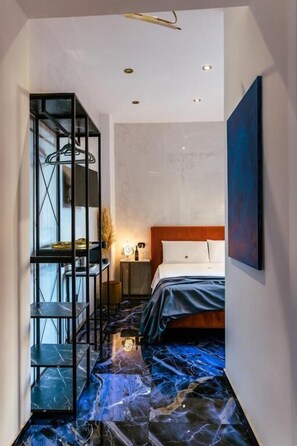 A modern hotel room with a marble floor, a bed with a wooden headboard, a black metal shelving unit, and a painting on the wall. - Marmur luxury room (Lecce)