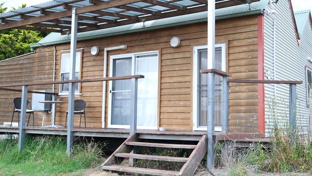 Eine Holzhütte mit verdeckter Veranda, einem kleinen Tisch und zwei Stühlen.