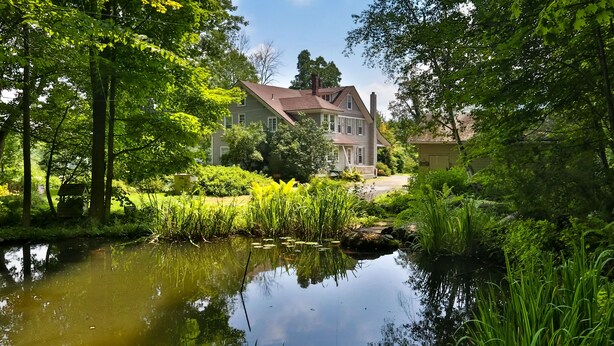 A large house with a pond in the foreground, surrounded by lush greenery and trees. - Rustic Log with Pool Game room Amazing koi pound just mins from Hunter Mountain (Elka Park)