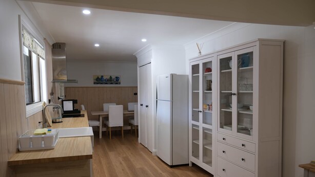 Une cuisine moderne avec un plancher en bois, des meubles blancs, un four encastré et un coin repas comprenant une table et des chaises.