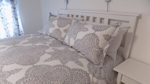 Un lit bien fait, avec une literie à motifs, une table de chevet dotée d’un tiroir et un luminaire fixé au mur.