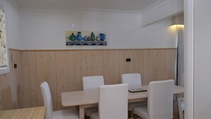 Un coin repas avec un mur lambrissé en bois, une table entourée de chaises blanches et un tableau décoratif au-dessus de la table.