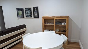 A dining area with a round white table and chairs, a wooden cabinet with dishes, and a black couch. - The Creekland Studio by Twodogfolly (Armidale)