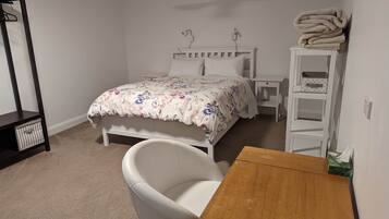 A bedroom with a bed, a chair, a wooden table, a white shelf, and a ceiling fan.