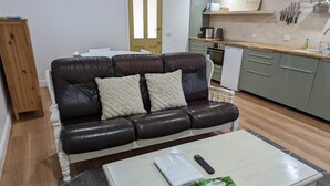 A living room with a dark brown leather sofa, a white coffee table, and a kitchen area with light green cabinets and a wooden countertop. - The Creekland Studio by Twodogfolly (Armidale)