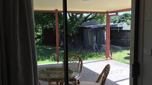Eine Glastür führt zu einer Terrasse mit einem Glastisch und Korbstühlen.