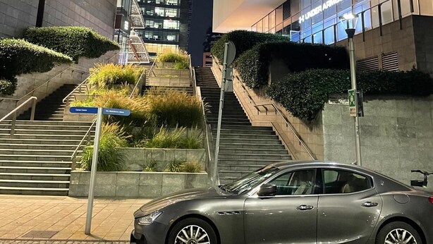 A modern building with a glass facade, a staircase leading to an upper level, and a car parked in front.