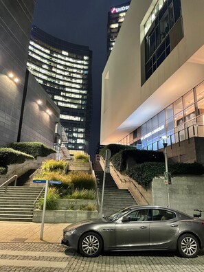 A modern building with a glass facade, a staircase leading to an upper level, and a car parked in front. - Mila by The Blue Twins Apartments Milano (Milano)