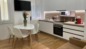 A modern kitchen with white cabinets, a microwave, and a sink. There is a dining table with chairs and a vase of flowers.