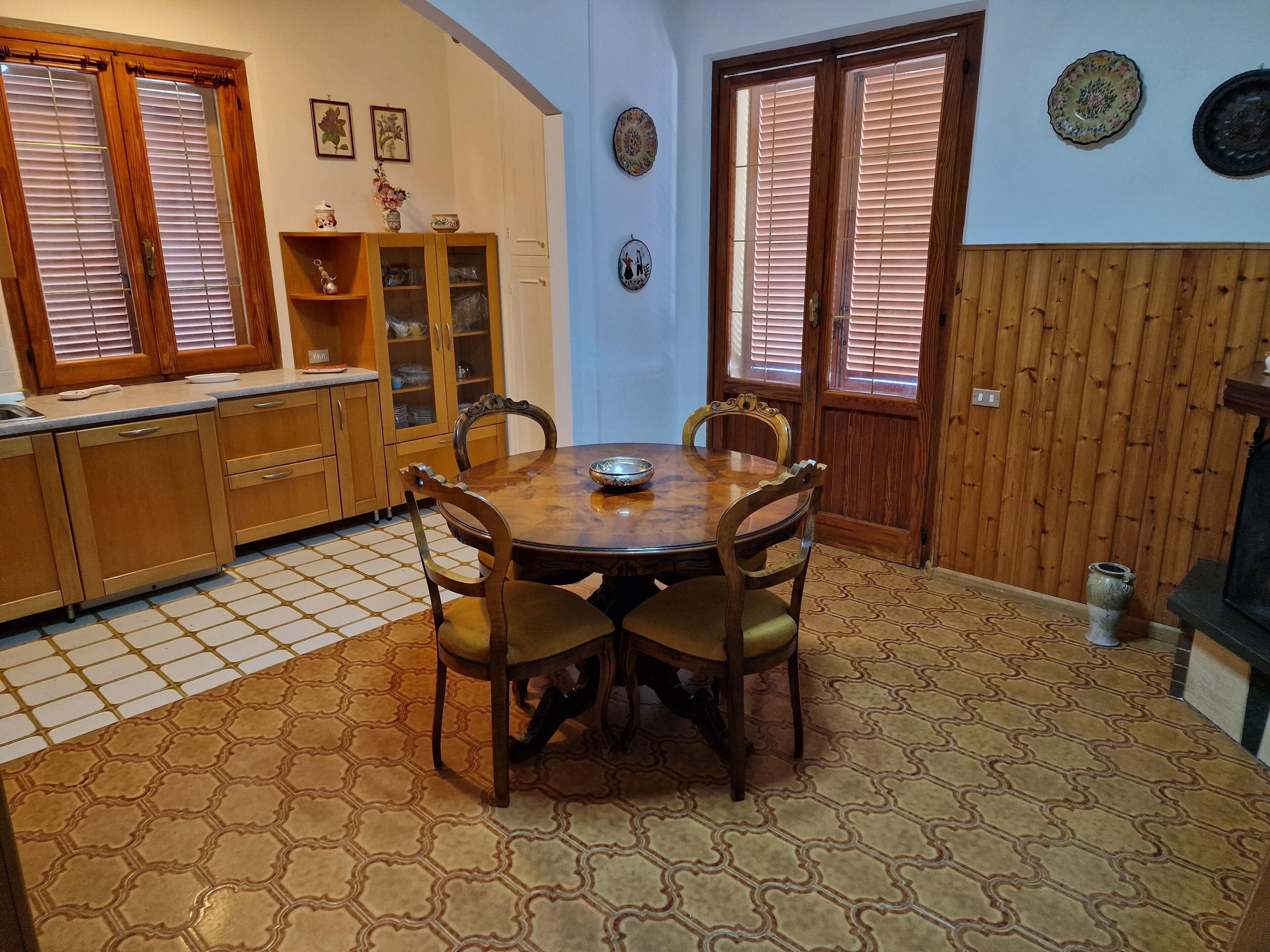 Un comedor con una mesa y sillas de madera, un mueble con puertas de vidrio y un piso de baldosas.