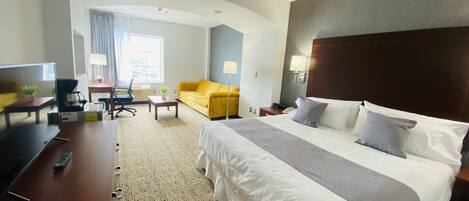 A hotel room with a large bed, a desk with a computer, a sofa, and a coffee maker.