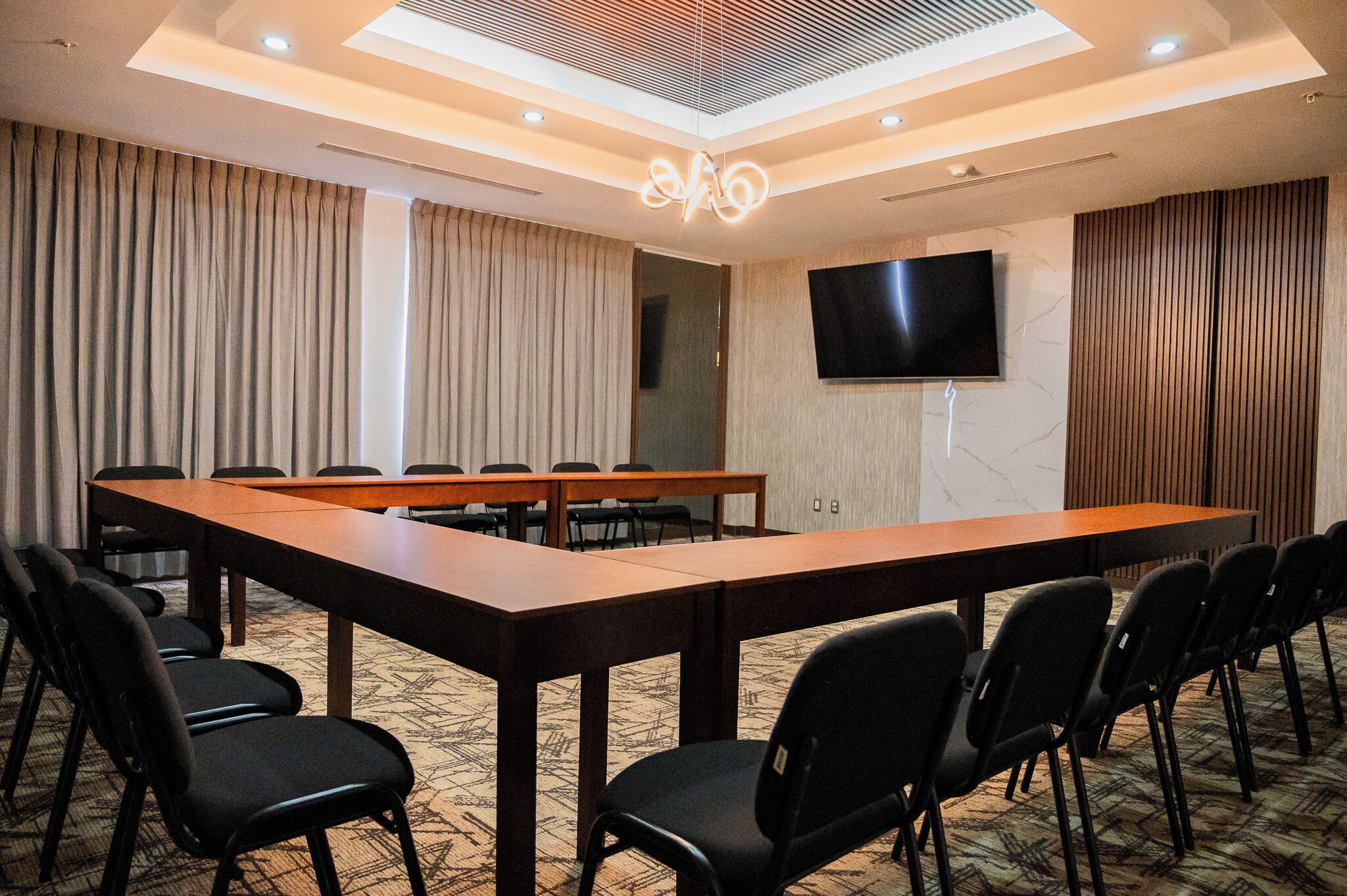 Une salle de conférence avec une longue table, des chaises, un téléviseur à écran plat et des rideaux.