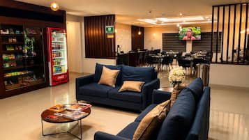 Un hall de hotel con una zona de estar, una máquina expendedora y una pantalla de televisión.