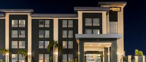 A multi-story hotel with a dark facade, multiple windows, and a well-lit entrance.