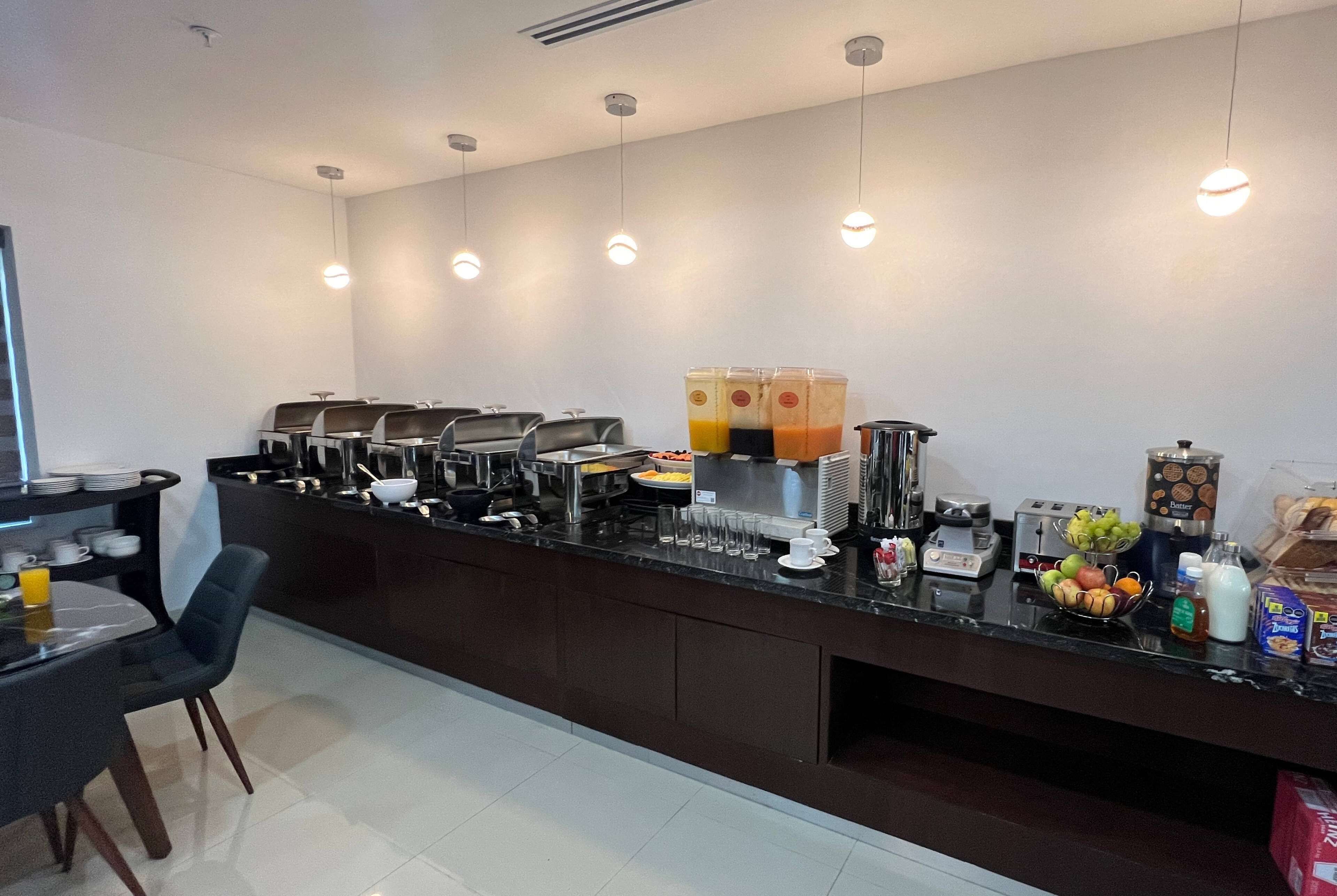 Una barra de desayuno moderna con varias parrillas, una estación de zumos y una variedad de productos para el desayuno.