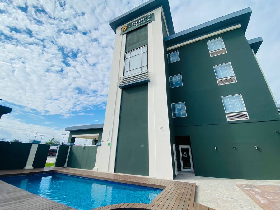 En modern hotellbyggnad med en swimmingpool, en täckt uteplats och en klar himmel.
