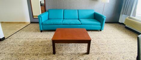 A living room with a teal sofa, a wooden coffee table, a large mirror, and a floor lamp.
