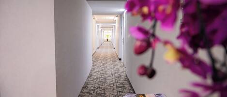 Un pasillo de hotel con alfombra estampada, un mostrador de recepción y una puerta al final.