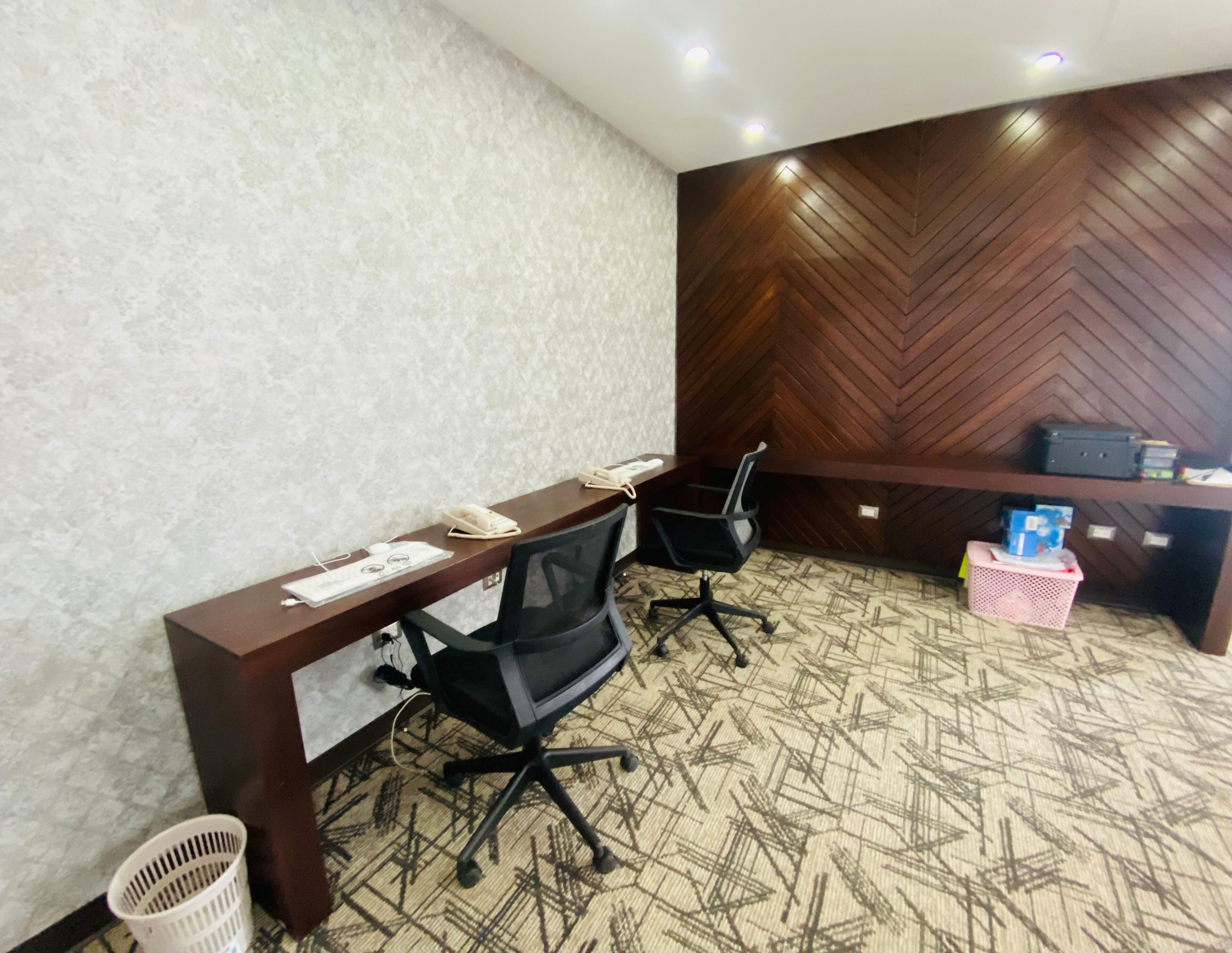 A conference room with a wooden desk, black office chairs, a patterned carpet, and a herringbone wall design.