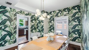 A dining area with a round table, white chairs, and a tropical leaf-patterned wallpaper.