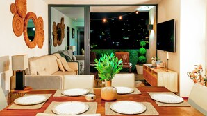 A dining area with a wooden table set for six, a sofa, and a TV mounted on the wall. - Altos Tower Apartamento de 3 habitaciones (San Salvador)