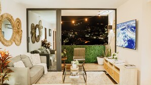 A modern living room with a sofa, coffee table, and a view of a cityscape at night. - Altos Tower Apartamento de 3 habitaciones (San Salvador)