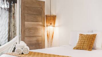 A neatly made bed with a woven blanket, a woven pillow, and rolled towels on a white bedspread.