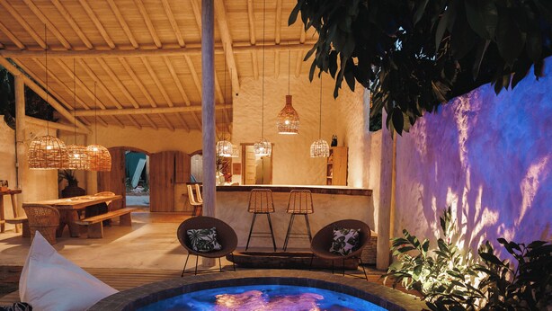 A hot tub area with a wooden deck, lounge chairs, and a bar area with hanging lights. - Pousada Villa Cacau (Porto Seguro)