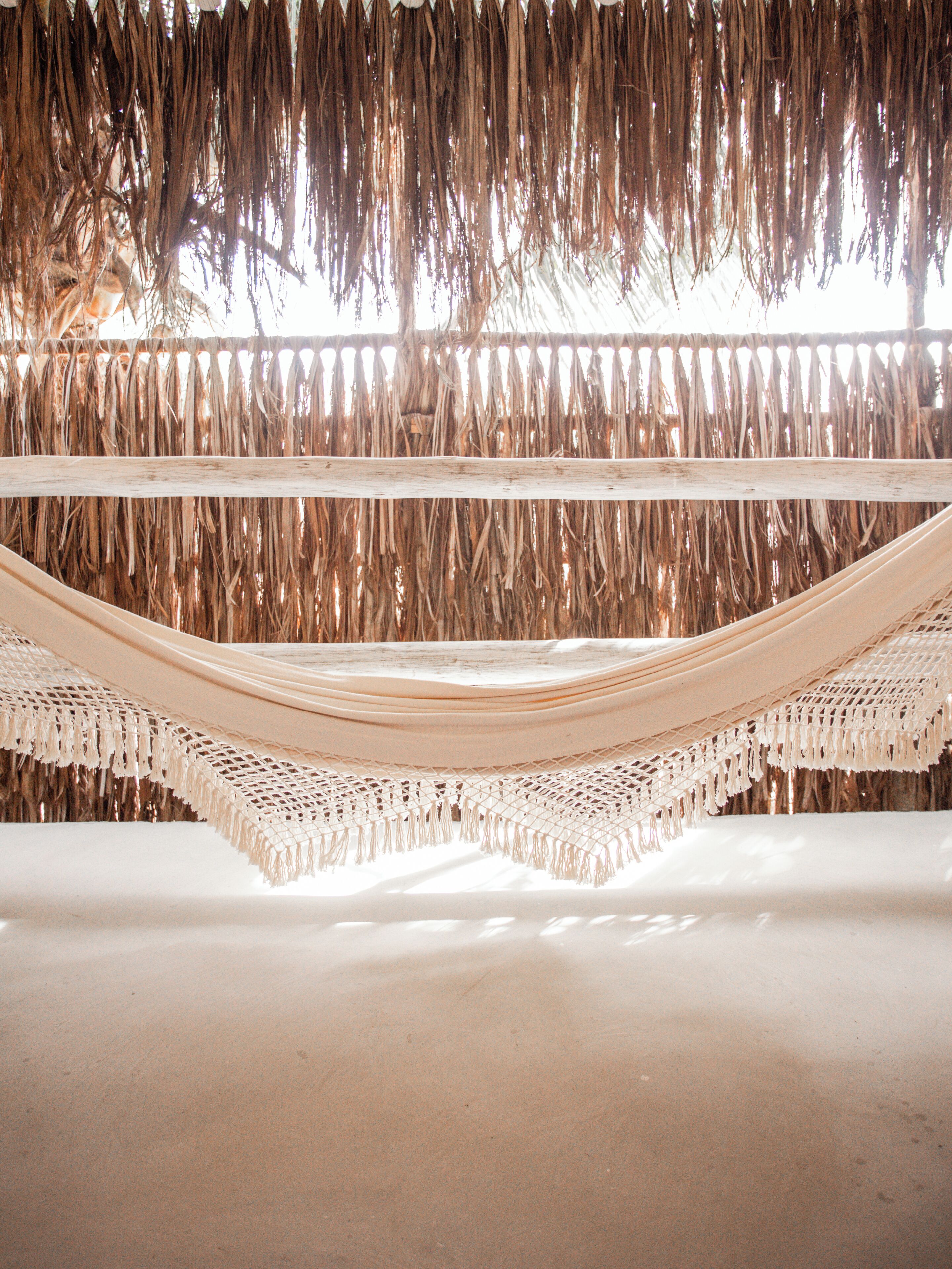 A hammock suspended between two wooden beams in a room with a sandy floor.