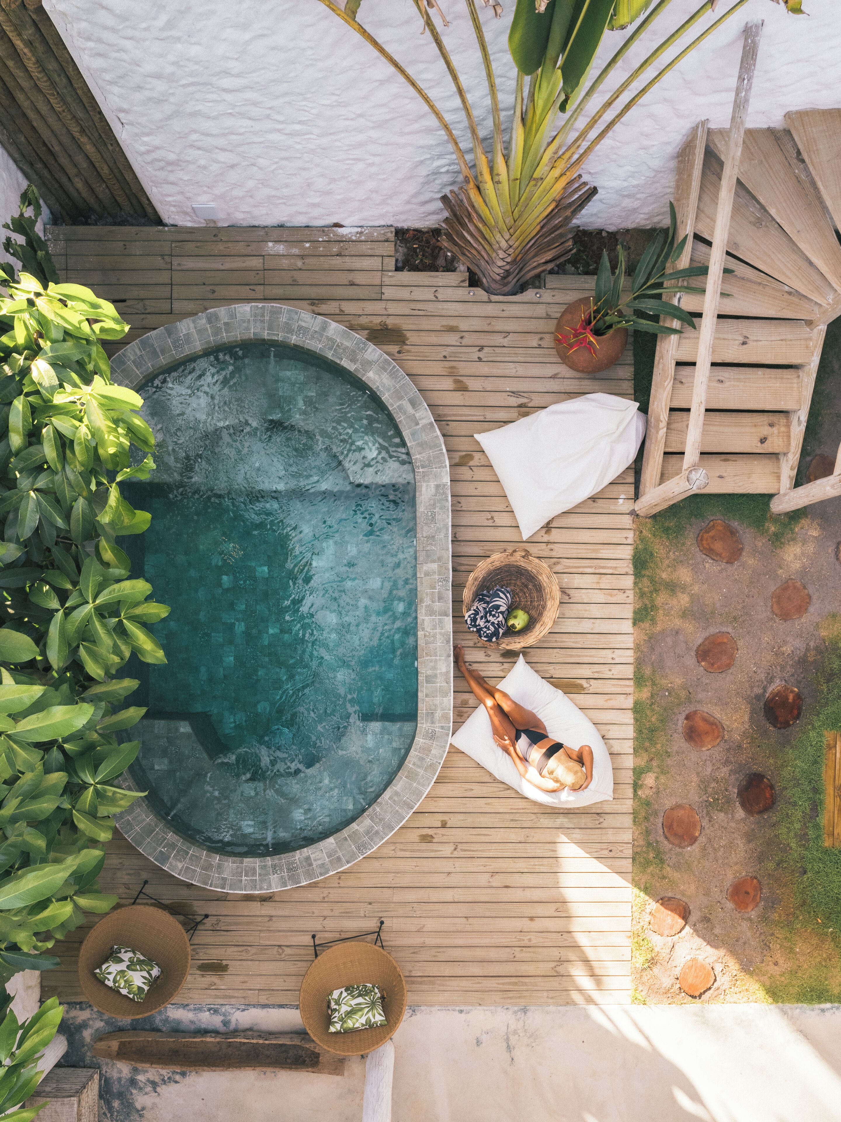 A hot tub surrounded by wooden decking, with a white wall in the background and potted plants nearby.