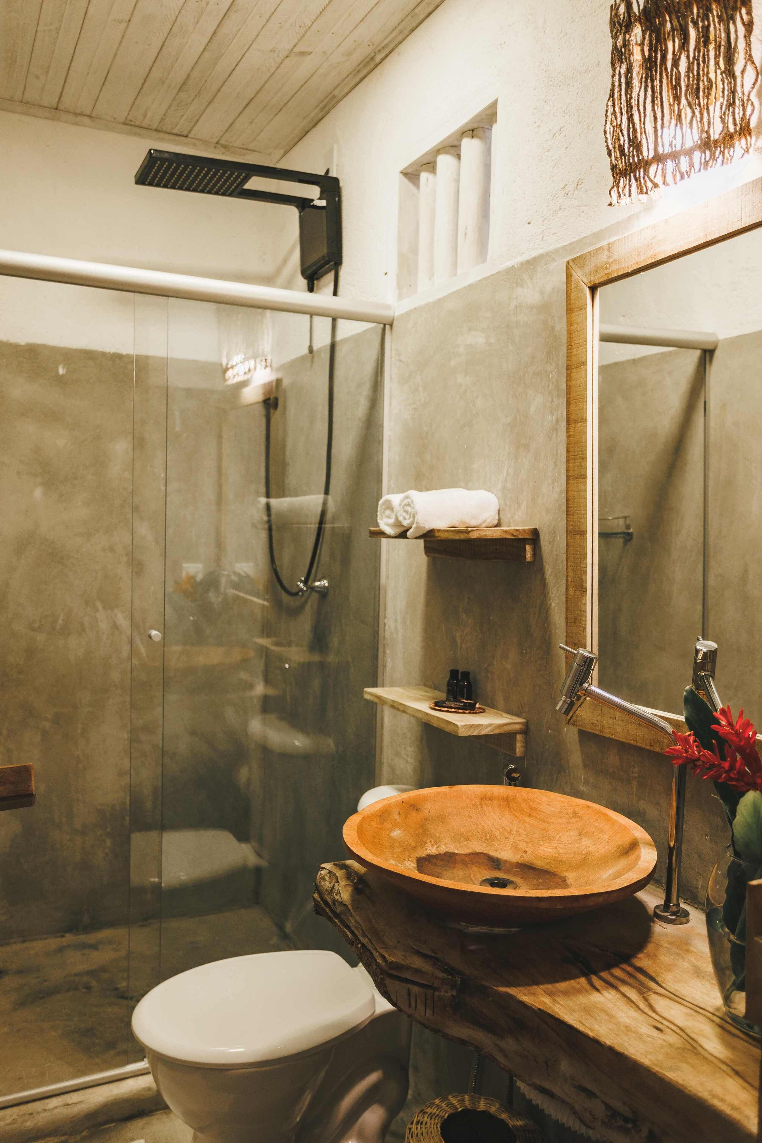 A bathroom with a glass-enclosed shower, a wooden vanity with a large bowl sink, a toilet, and a mirror.