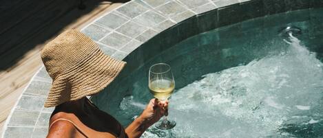 Una mujer relajándose en un jacuzzi, con una copa de vino, rodeada de hielo y un bol con una botella y una flor.
