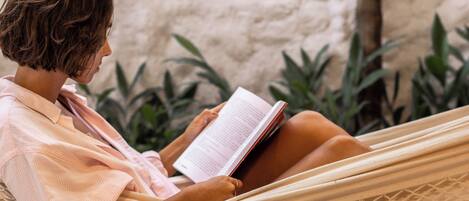 A person relaxing in a hammock with a book, set against a textured wall and greenery.