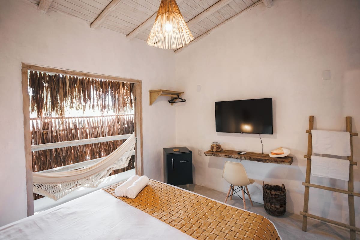 A bedroom with a bed, a hammock, a TV, a desk, and a ladder.