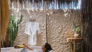 A person relaxing in a bathtub with a tray of fruits and a white robe hanging on the wall. - Pousada Villa Cacau (Porto Seguro)